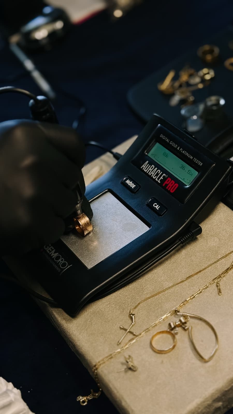 Anel de ouro sendo testado no aparelho digital de teor, com a mão do Carlos enluvada